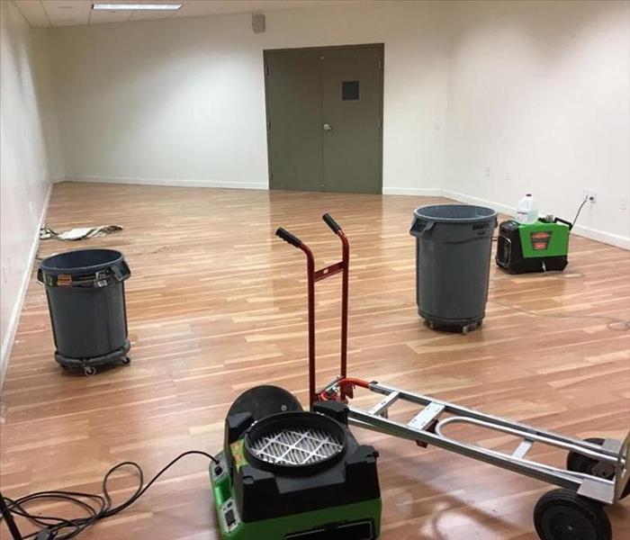 Large room with white walls and wood flooring. Some drying equipment not yet in use scattered across the floor