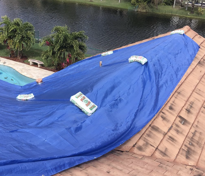 roof with blue tarp over it being help in place by heavy bags of sand